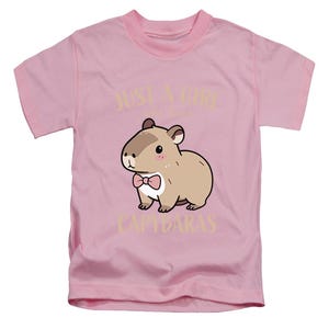 May include: Pink t-shirt featuring a cartoon capybara wearing a pink bow tie. The text "JUST A GIRL who loves CAPYBARAS" is printed above and below the capybara illustration. The shirt has short sleeves and a crew neck.
