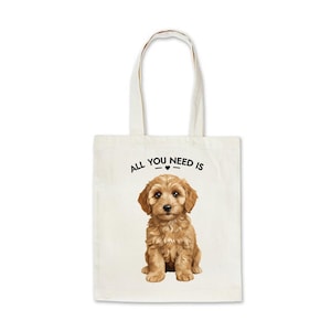 May include: Cream tote bag with a light brown puppy illustration. The text "ALL YOU NEED IS" is printed above the puppy in black. The bag has two cream-coloured handles.