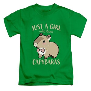 May include: Green t-shirt with the text "JUST A GIRL who loves CAPYBARAS". The shirt features a cartoon capybara wearing a pink bow tie. The capybara is brown with a white belly.