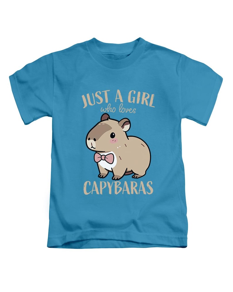 May include: A light blue t-shirt featuring a cartoon capybara with a pink bow tie. The text reads "JUST A GIRL who loves CAPYBARAS" in a light brown color. The shirt is designed for children.