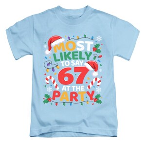 May include: Pale blue t-shirt featuring the phrase "MOST LIKELY TO SAY 67 AT THE PARTY". The design incorporates festive elements like Santa hats, candy canes, and fairy lights, perfect for a Christmas celebration.