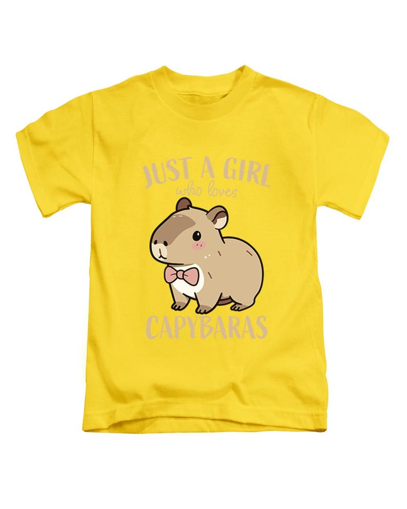 May include: A yellow t-shirt featuring a cartoon capybara wearing a pink bow tie. The text "JUST A GIRL who loves CAPYBARAS" is printed above and below the capybara illustration. The shirt is made of a soft material.