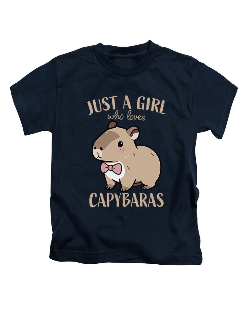 May include: Navy blue t-shirt featuring a cartoon capybara wearing a pink bow tie. The text "JUST A GIRL who loves CAPYBARAS" is printed above and below the capybara illustration. The shirt is designed for children.