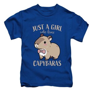 May include: Blue t-shirt with the text "JUST A GIRL who loves CAPYBARAS." The shirt features a cartoon capybara wearing a pink bow tie. The capybara is brown with a white belly and pink cheeks.