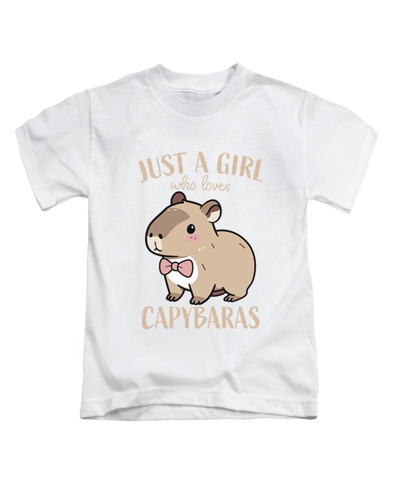 May include: White t-shirt featuring a cartoon capybara wearing a pink bow tie. The text reads "JUST A GIRL who loves CAPYBARAS" in a light brown color. The design is centered on the front of the shirt.