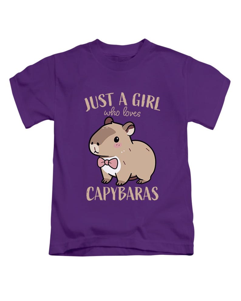 May include: Purple t-shirt featuring a cartoon capybara with a pink bow tie. The text reads "JUST A GIRL who loves CAPYBARAS" in a light brown color. The design is centered on the front of the shirt.
