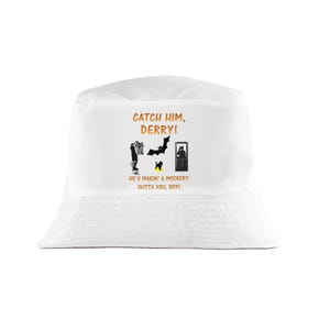 May include: A white bucket hat featuring orange text that reads CATCH HIM, DERRY! HE'S MAKIN' A MOCKERY OUTTA YOU, BOY! The design includes black silhouettes of a person holding a garment, a bat, a small dog, and a person looking into a mirror.