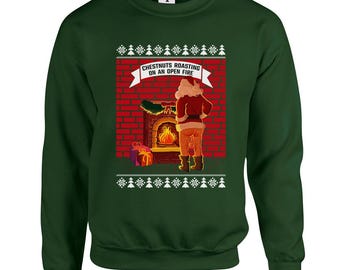 Puede incluir: Sudadera verde oscuro con un gráfico navideño. El gráfico representa a Papá Noel asando castañas frente a una chimenea. El texto "Chestnuts Roasting on an Open Fire" se muestra encima de la chimenea. La sudadera tiene un patrón festivo.