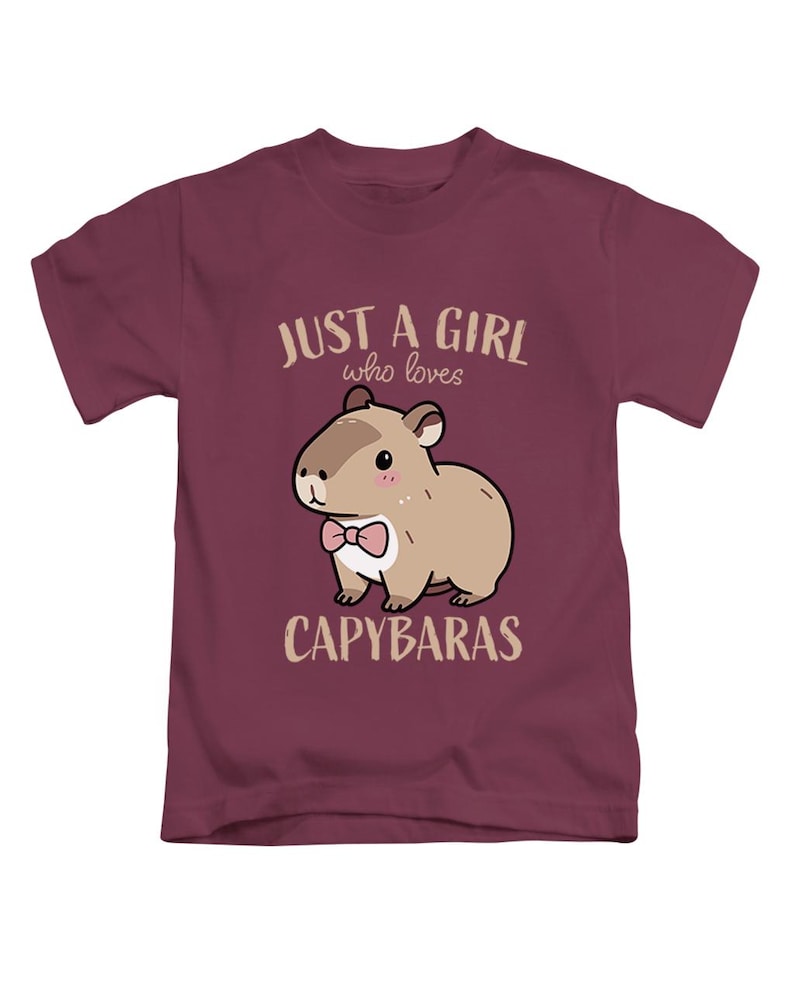 May include: A maroon t-shirt featuring a cartoon capybara wearing a pink bow tie. The text "JUST A GIRL who loves CAPYBARAS" is printed above and below the capybara illustration. The shirt is made of a soft material.