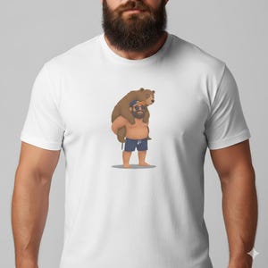May include: White t-shirt featuring a cartoon illustration of a man carrying a brown bear on his shoulders. The man is wearing blue swim trunks and sunglasses. The bear is also wearing sunglasses. The design is centered on the shirt.