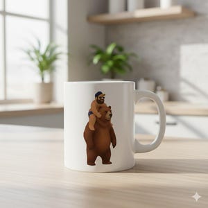 May include: White ceramic mug featuring a cartoon illustration of a person riding a brown bear. The person is wearing a blue cap and sunglasses. The bear is standing upright. The mug has a white handle and is set against a kitchen background.