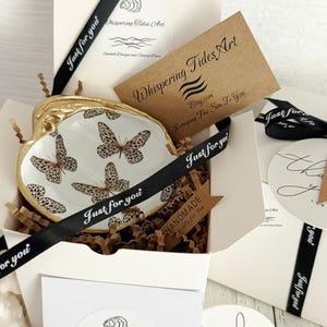 May include: A decorative seashell-shaped dish with a gold rim and butterfly design, presented in a white gift box with black ribbon that says "Just for you". The box includes a handmade tag and a card from Whispering Tides Art.