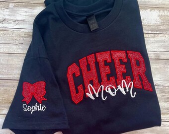 May include: Black t-shirt with red glitter "Cheer Mom" text and a red bow with "Sophie" text on the sleeve.