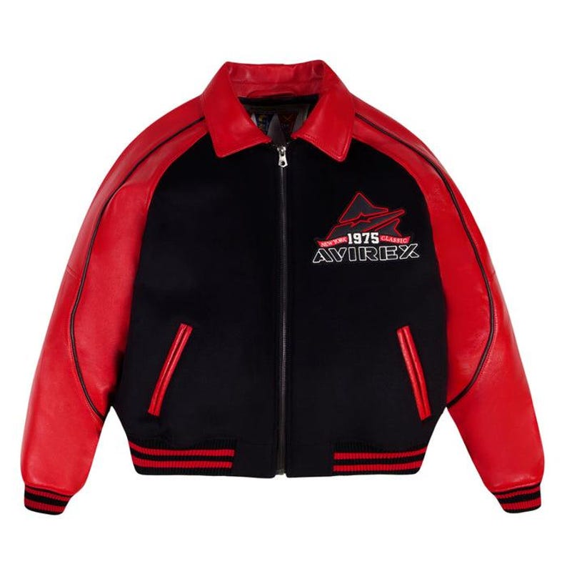 May include: A black and red varsity jacket featuring a fold-down collar, a full-length front zipper, and long sleeves. The chest displays an embroidered logo with the text "NEW YORK 1975 CLASSIC AVIREX". It includes two side pockets and ribbed cuffs.
