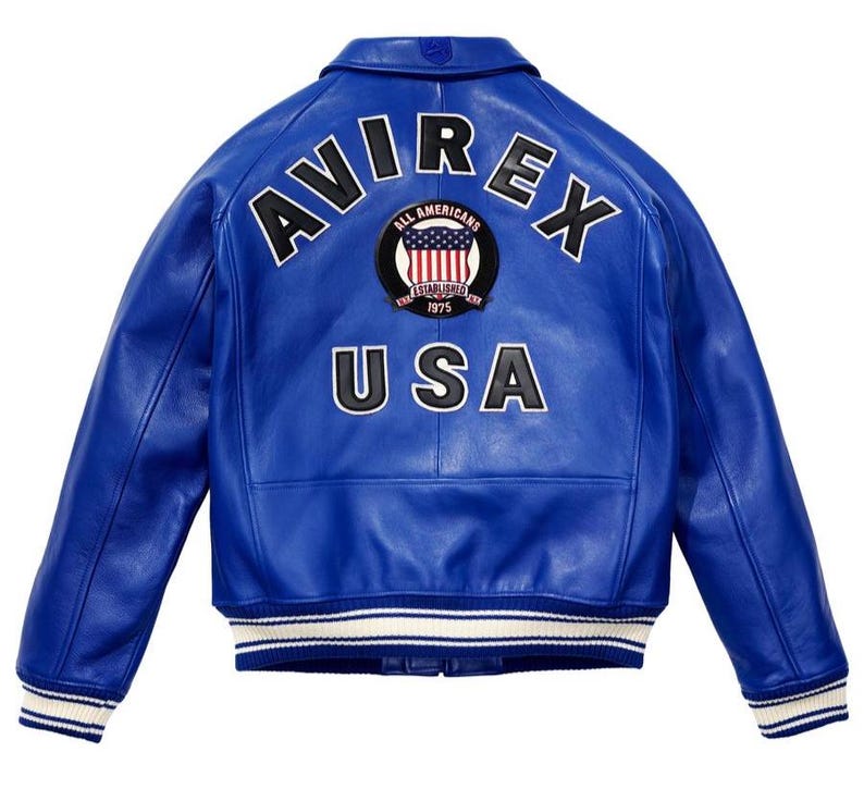 K&ouml;nnte beinhalten: K&ouml;nigsblaue Lederjacke mit dem Wort "AVIREX" in wei&szlig;en Buchstaben &uuml;ber den Schultern. Darunter befindet sich ein kreisf&ouml;rmiger Aufn&auml;her mit der Aufschrift "ALL AMERICANS ESTABLISHED 1975 USA". Die Jacke hat einen wei&szlig;-blauen Streifen.