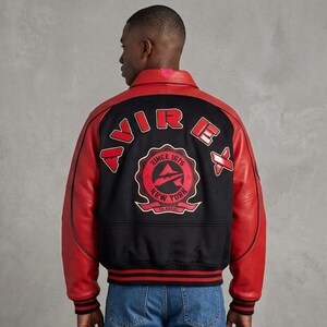 May include: A black and red varsity jacket featuring red leather sleeves and a black wool-blend body. The back displays the text AVIREX in red lettering above a circular patch with the text SINCE 1975 NEW YORK and an airplane graphic.