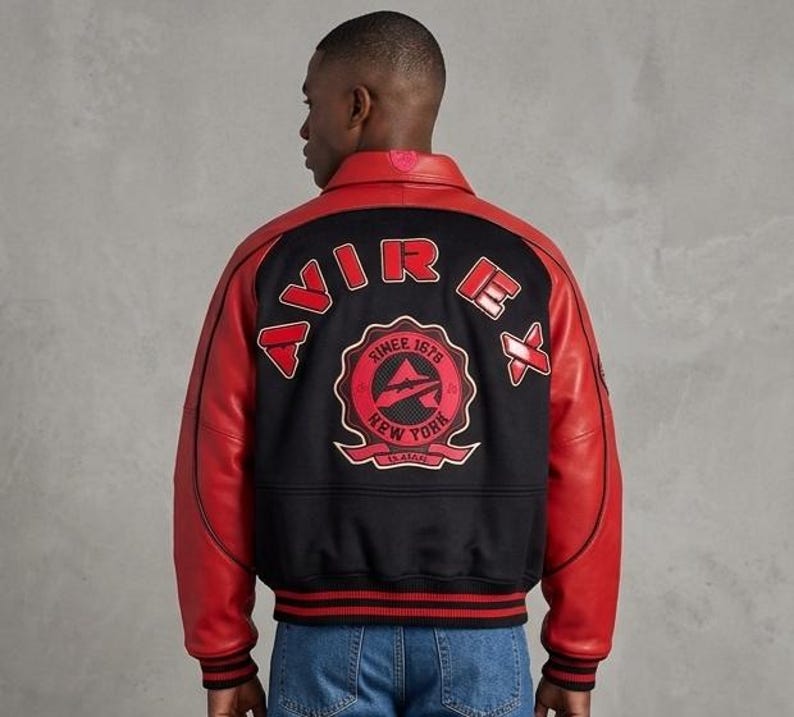 May include: A black and red varsity jacket featuring red leather sleeves and a black wool-blend body. The back displays the text AVIREX in red lettering above a circular patch with the text SINCE 1975 NEW YORK and an airplane graphic.