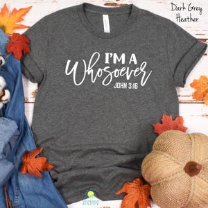 Puede incluir: Camiseta gris oscuro jaspeado con el texto "I'M A Whosoever JOHN 3:16" en escritura blanca. La camiseta es de cuello redondo. La imagen incluye decoraciones de temática otoñal, como hojas y una calabaza.