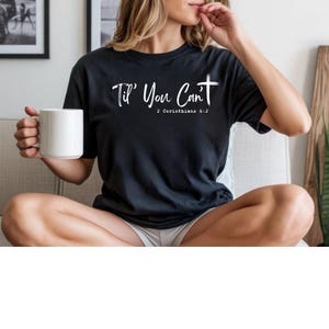 May include: Black t-shirt with the text "Til' You Can't" and a cross graphic. The text "2 Corinthians 6:2" is below the main text. A white coffee mug is held in the left hand.