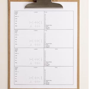 May include: A clipboard with a silver metal clip holding a white sheet of paper. The paper has a grid of boxes with lines and text. The clipboard is made of brown cardboard.