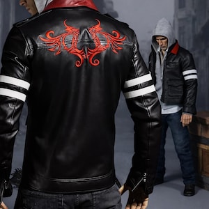 Könnte beinhalten: Schwarze Lederjacke mit roter Stickerei auf dem Rücken und weißen Streifen auf den Ärmeln. Die Jacke hat einen roten Kragen und einen Reißverschluss. Das Model trägt dunkle Jeans.