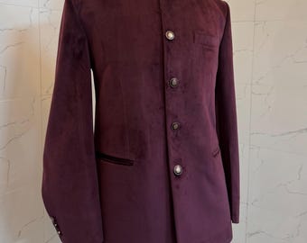 May include: A burgundy velvet jacket with a mandarin collar and gold-coloured buttons. The jacket has a tailored fit and a single chest pocket. The garment is displayed on a mannequin against a neutral background.