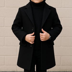 Könnte beinhalten: Ein junges Kind in einem schwarzen Mantel, Rollkragenpullover und Hose. Das Kind trägt auch schwarze Stiefel und eine Uhr. Das Bild enthält den Text "TEXTTHRIVE TAILORING MENS & WOMEN SUITS" in der oberen linken Ecke.