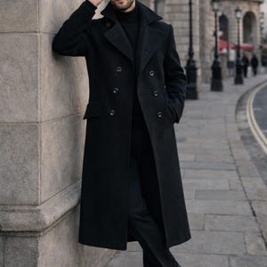 Puede incluir: Un abrigo largo negro de doble botonadura con solapas anchas. El abrigo se lleva sobre un cuello alto negro y pantalones negros. La persona lleva gafas de sol negras y zapatos de cuero negros. La imagen está tomada al aire libre.