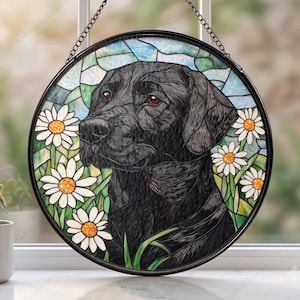 May include: A circular stained glass suncatcher featuring a black Labrador retriever portrait surrounded by white daisies with yellow centers against a light blue and green background, suspended by a thin black metal chain.