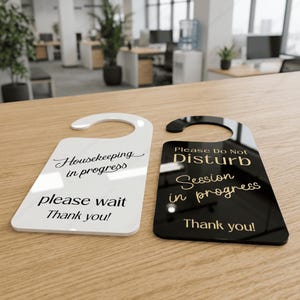 May include: Two door hangers with hook tops. The white hanger features black text reading Housekeeping in progress, please wait, Thank you!. The black hanger features gold text reading Please Do Not Disturb, Session in progress, Thank you!.