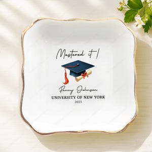 May include: A white ceramic square dish with a gold rim. The dish features a graduation cap and scroll illustration with the text "Mastered it!" and personalized details: name, university, and year.