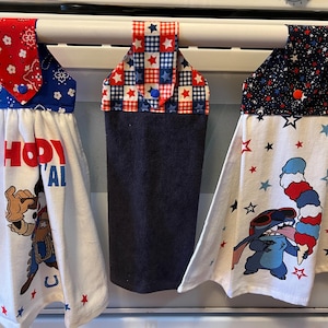May include: Three kitchen towels with patriotic designs hanging on an oven. The towels feature red, white, and blue patterns. One towel has a cowboy graphic and the text "Howdy Y'all". Another has a Stitch graphic with an ice cream cone.