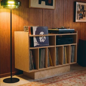 Groove No.3 birch plywood record player stand with vinyl storage, turntable, amplifier shelf, and records in a warm wood-paneled listening room.
