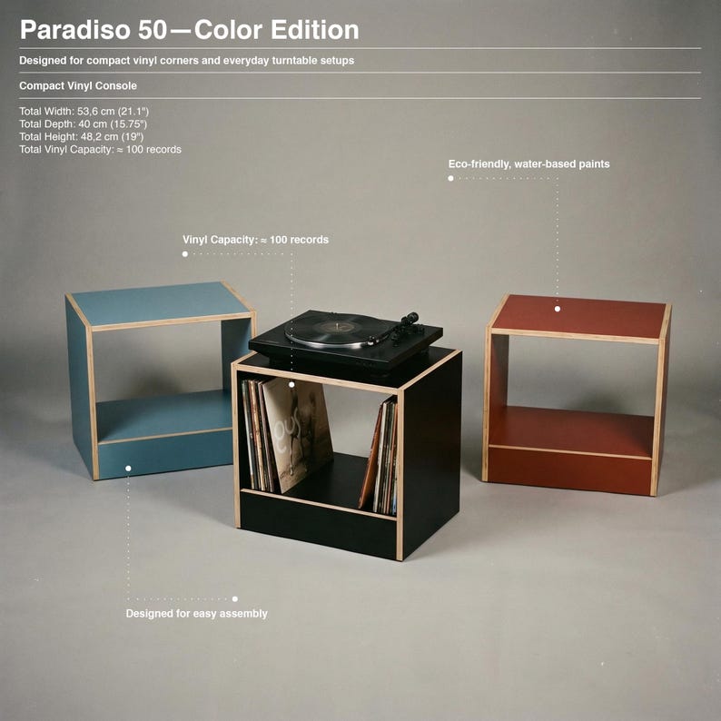 Paradiso 50 Color Edition modular plywood record player stand and vinyl storage unit shown as an infographic against a gray background. The black center unit holds a turntable and upright records. Chalk blue and oxide red modules stand on each side. The text says compact vinyl console. Width 53.6 cm. Depth 40 cm. Height 48.2 cm. About 100 record capacity. Water based paints. Designed for easy assembly.