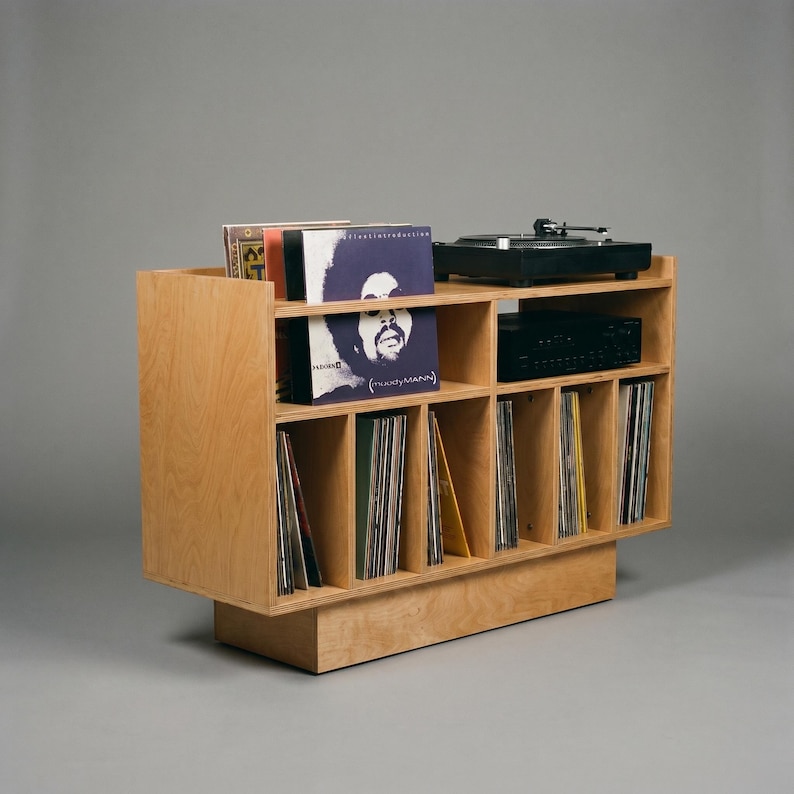 Angled view of Groove No.3 birch plywood record player stand with turntable, amplifier shelf, front-facing album display, and organized vinyl storage compartments.