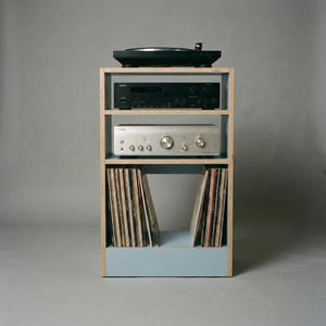 Modular plywood record player stand made from 18mm plywood with a chalk blue finish on the lower section and natural plywood edges. A black turntable sits on top with two stereo components on the shelves below and vinyl records stored upright in the bottom compartment.