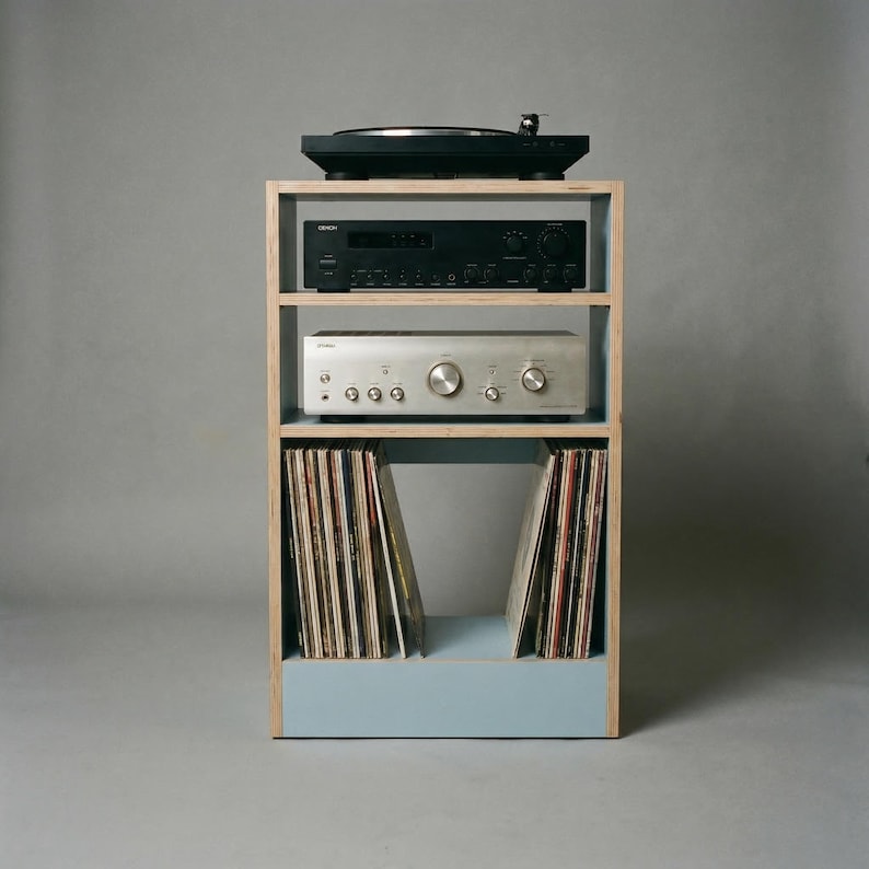Modular plywood record player stand made from 18mm plywood with a chalk blue finish on the lower section and natural plywood edges. A black turntable sits on top with two stereo components on the shelves below and vinyl records stored upright in the bottom compartment.