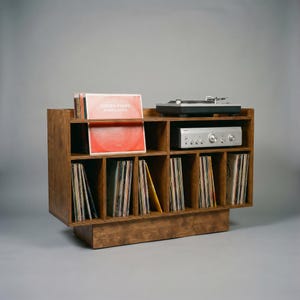 Side angled view of Groove No.3 walnut vinyl console showing warm wood grain, turntable platform, open audio shelf, displayed records, and organized LP storage sections.