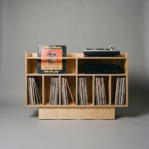 Front view of Groove No.3 birch plywood turntable console with a Stevie Wonder record on display, audio equipment shelf, and six vertical vinyl storage compartments.