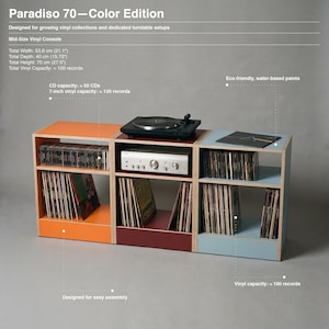 Paradiso 70 Color Edition product infographic showing a low three unit modular plywood vinyl console in orange oxide red and chalk blue against a gray background. A turntable sits on the center unit above an amplifier. Shelves store LPs and CDs. Text highlights Mid Size Vinyl Console. Width 53.6 cm. Depth 40 cm. Height 70 cm. Vinyl capacity about 100. CD capacity about 50. 7 inch vinyl capacity about 130. Eco friendly water based paints.