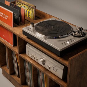 Close-up of Groove No.3 walnut record player console showing turntable placement, silver amplifier, layered plywood edges, record display slots, and vinyl storage below.