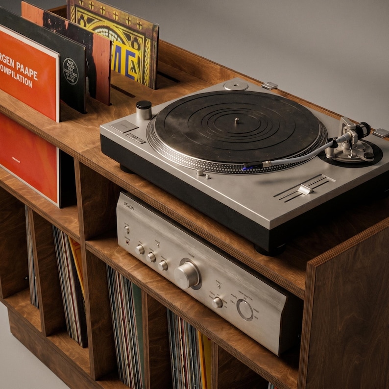 Close-up of Groove No.3 walnut record player console showing turntable placement, silver amplifier, layered plywood edges, record display slots, and vinyl storage below.