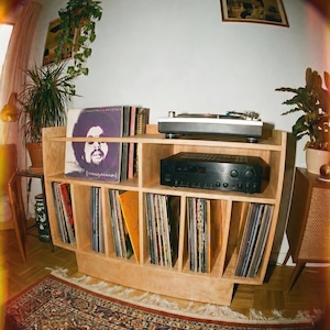 Groove No.3 birch plywood record player stand with turntable, amplifier shelf, vinyl records, houseplants, and a patterned rug in a cozy home listening corner.