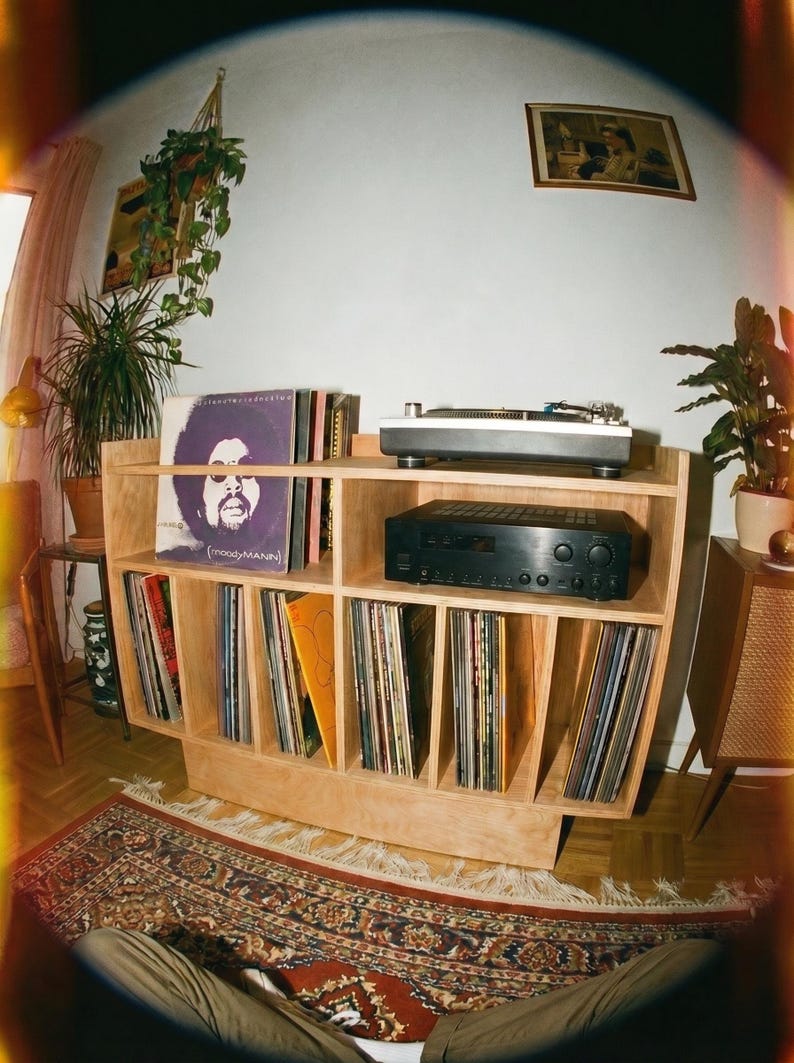 Groove No.3 birch plywood record player stand with turntable, amplifier shelf, vinyl records, houseplants, and a patterned rug in a cozy home listening corner.