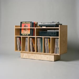 Angled studio view of Groove No.3 record player stand with light birch plywood grain, turntable shelf, receiver space, front album display, and vinyl storage compartments.