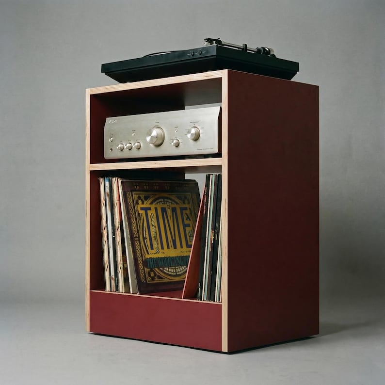 Modular plywood record player stand in oxide red with natural plywood edges shown from a front angled view against a gray background. A black turntable sits on top with a silver stereo component below and vinyl records stored upright in the lower section.