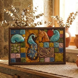 Puede incluir: Una obra de arte enmarcada en baldosas de cerámica con un pavo real, una cabeza de caballo y otros elementos decorativos en tonos azules, marrones y rojos. La obra se exhibe sobre una superficie de madera con macetas de terracota al fondo.