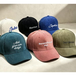 May include: Six corduroy baseball caps in cream, black, blue, teal, pink, and olive green. Each cap features embroidered text on the front, including the names Jake, Harrison, and Sophia, plus the phrases Add your own design, Personalized Hat, and Your Words.