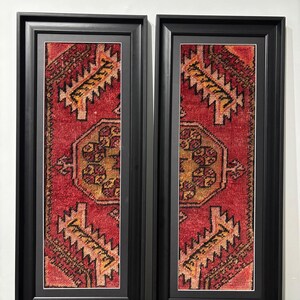 Pode incluir: Duas obras de arte de parede retangulares emolduradas. Cada uma apresenta uma se&ccedil;&atilde;o de um tapete padronizado em vermelho, dourado e preto. As molduras s&atilde;o pretas com um passe-partout branco. O design do tapete inclui formas geom&eacute;tricas e detalhes intrincados.