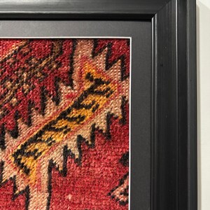 Pode incluir: Close-up de uma obra de arte t&ecirc;xtil emoldurada. A obra apresenta um padr&atilde;o intrincado e vibrante em tons de vermelho, amarelo e preto. A moldura &eacute; um design retangular preto simples, proporcionando uma borda limpa para a obra de arte.